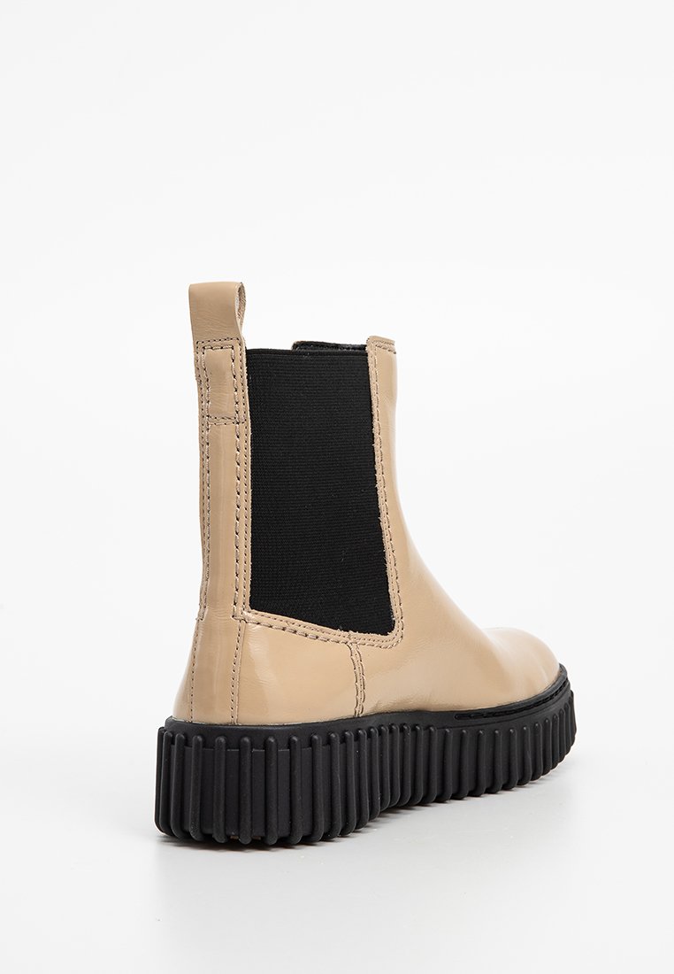 Stivale ankle in pelle beige con un pannello elastico laterale nero, punta rotonda e suola in gomma nera testurizzata. Presenta un'etichetta a fibbia sul retro.