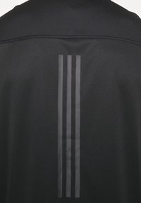 Tissu noir avec trois bandes réfléchissantes verticales gris foncé centrées dans le dos, sous la couture de l'épaule.