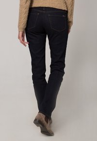 Jeans de mezclilla azul oscuro con forma ajustada, con detalles de costura sutiles, bolsillos traseros y combinados con botas de tobillo marrón claro.