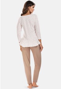 Weißes Oberteil mit rosa und grauen Punkten, gerafftem Saum, kombiniert mit beigen Hosen. Weicher Stoff, lange Ärmel, lässige Passform.
