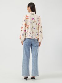 Blomstret bluse i kremfarge med puff ermer og høy krage, kombinert med blå vide jeans og svarte hæler.