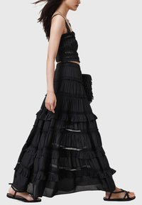 Ensemble crop top court noir à volants et jupe, design à couches avec bordure en dentelle, tissu fluide, associé à des sandales plates noires, sac porté sur le côté.