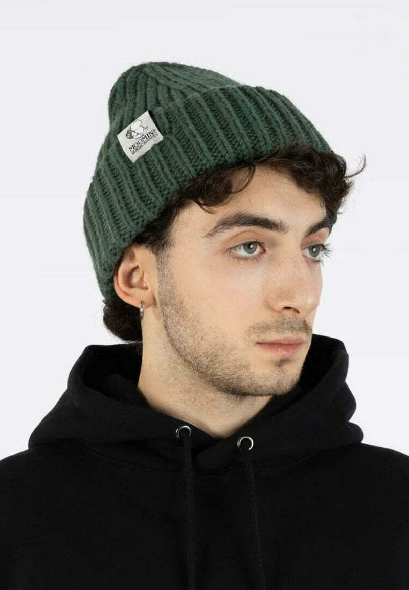 Nuorodas žmogus su šviesia oda ir trumpais garbanotais plaukais, dėvintis tamsiai žalią megztinę ir juodą džemperį, žiūri šiek tiek į dešinę nuo kameros.