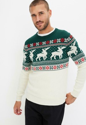 Pull en tricot vert avec un fond blanc, présentant un motif de renne et de flocons de neige en rouge, vert et blanc. Col rond et poignets côtelés.