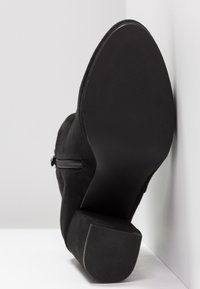 Sort suede ankelstøvle med en sidelukning, der har en struktureret gummisål og en let firkantet tådesign.