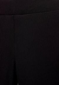 Tissu noir à côtes avec une surface texturée, présentant des rayures verticales. Le matériau semble extensible et ajusté.