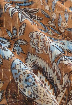 Hnedá látka s kvetinovými a vtáčími vzormi v modrej a krémovej farbe, s vertikálnymi zlatými pruhmi, ktoré vytvárajú textúrovaný vzhľad.