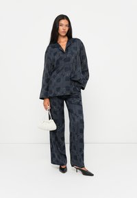 Navy patterned two-piece outfit featuring a loose-fitting shirt with a collar and matching wide-leg pants. Accessories include a white handbag.