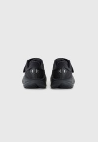 Baskets de sport noires avec une tige texturée, une sangle Velcro et un col rembourré. Les accents réfléchissants au niveau du talon améliorent la visibilité.