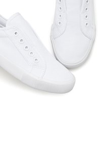 Weiße Leinenschlupfsneaker mit Gummisohlen, die eine glatte Textur, eine runde Zehenpartie und mehrere Ösen an den Seiten aufweisen.