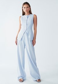 Heleheline sansvarrukatega topp, millel on nööpide esiosa ja peplum-konstruktsioon, mis on kombineeritud laia jalaga pükstega samas värvitoonis. Sile kangastekstuuri.