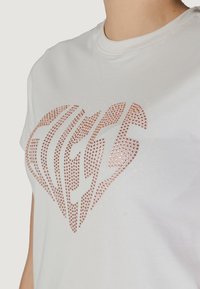 T-shirt bianco in cotone con un grande design a forma di cuore in strass rosa oro, con finitura testurizzata e scollo rotondo.