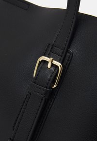 Musta nahkainen käsilaukkuremmi, jossa on kultainen metallinen solki. Remmi on varustettu tekstuuripinnalla ja saumurisaumadetailleilla, jotka parantavat sen muotoilua.