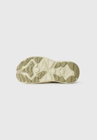 Semelle de chaussure avec une surface en caoutchouc texturé beige et vert clair, présentant un design de grip en relief et des éléments de semelle proéminents.