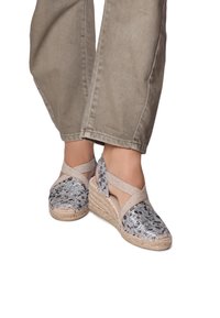 Wedge espadrilles with a metallic snake print upper, beige fabric straps, and jute-wrapped soles. Textured finish and open design.