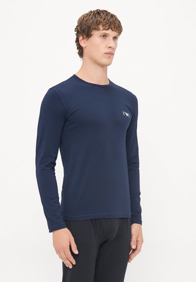 Lange ermede marineblå t-skjorte laget av glatt stoff, med rund hals og en liten logo på brystet. Tilsittende design.