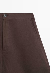 Brown fabric skirt with side pockets, button closure, and visible stitching on a white background.