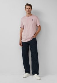 Helles rosa Baumwoll-T-Shirt mit Rundhalsausschnitt und kurzen Ärmeln, kombiniert mit dunkelblauen Jeans und weißen Sneakern.