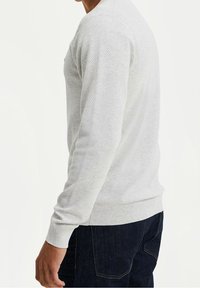 Ljusgrå stickad tröja med ett strukturerat mönster och ribbade muddar, kombinerad med mörka jeans, visad från sidan.