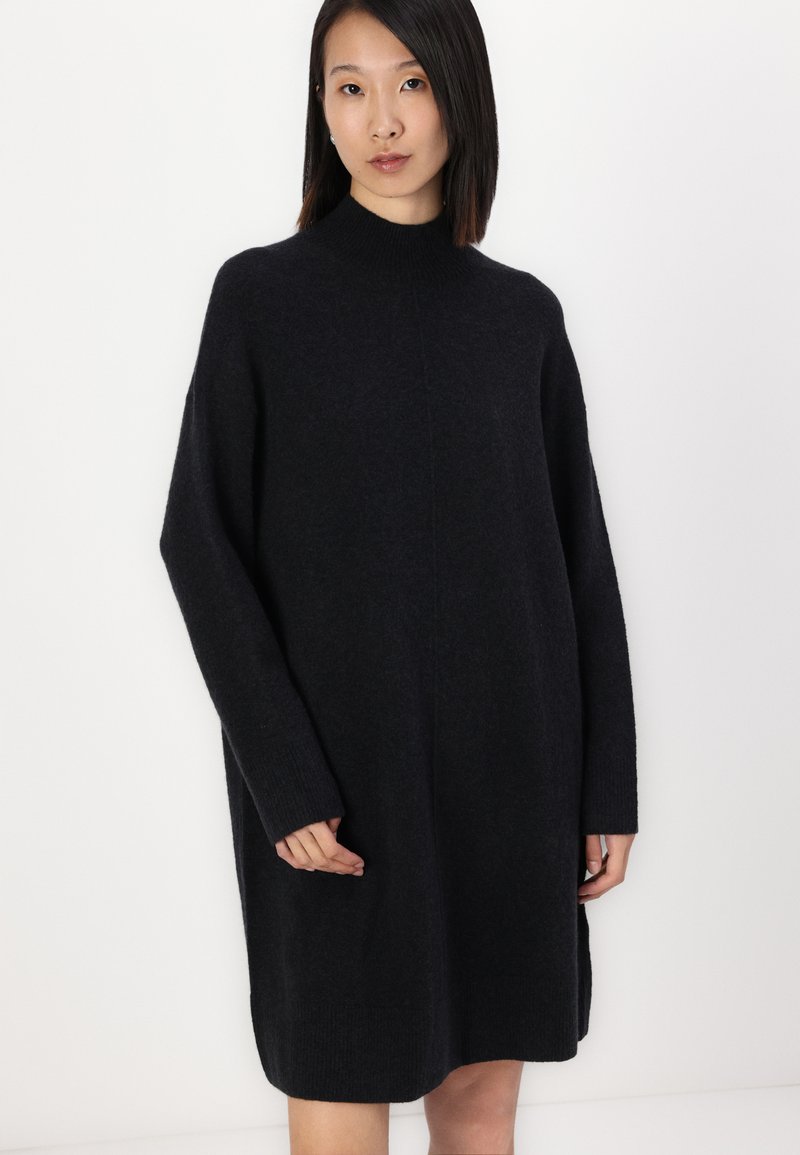 Schwarzes Strickkleid mit hohem Ausschnitt, weiten Ärmeln und seitlichen Taschen. Verfügt über eine weiche Textur und eine lockere, übergroße Passform.