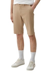 Beige shorts gemaakt van lichte stof, met zijzakken en een getailleerde pasvorm, gecombineerd met witte sokken en sneakers.