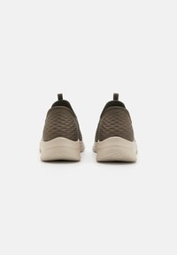 Mørke olivengrønne sneakers med en teksturert overflate, beige såler og hemper bak. Rund form med et fleksibelt design.