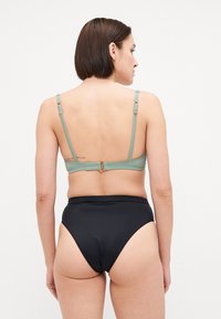 Top bikini a coste di colore verde menta con spalline regolabili e dettagli in oro, abbinato a un bikini bottom nero a vita alta.