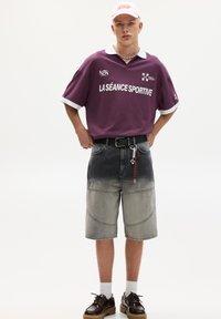 Purple oversized polo with white collar, featuring text "LA SÉANCE SPORTIVE." Worn with knee-length gradient gray shorts and brown shoes.