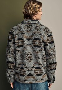 Gray fleece jacket with black and brown geometric patterns, featuring a collared neckline and textured fabric. Back view displays loose fit.