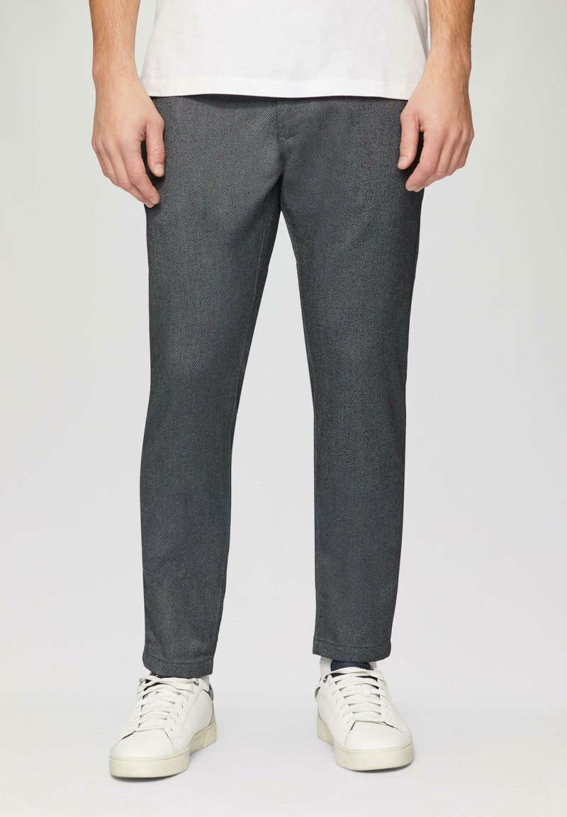 Pantalons tissés gris à coupe slim, avec une légère texture et des poches latérales, associés à des baskets blanches.