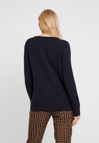 Navyblauwe trui met een ronde hals, ribbels aan de mouwen en zoom, weergegeven met geblokte bruine en oranje broek. Een gladde textuur, casual pasvorm.
