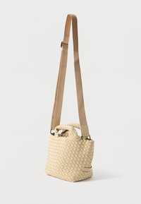 Πλεκτή μπεζ τσάντα χειρός με υφή, που διαθέτει καμπυλωτή κορυφαία λαβή και ρυθμιζόμενο μπεζ ιμάντα, παρουσιάζοντας μια συμπαγή, ορθογώνια μορφή.