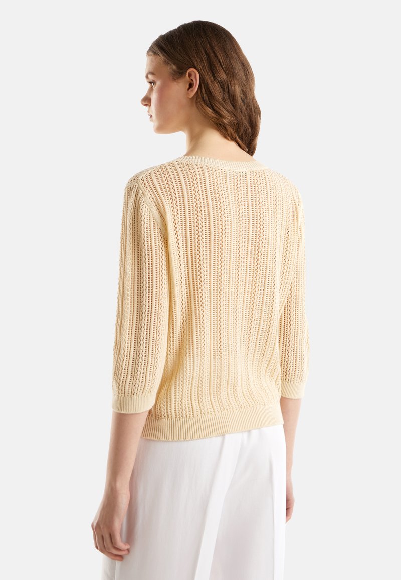 Jasnożółty, dzianinowy sweter z teksturowanym, ażurowym wzorem. Posiada rękawy do łokci oraz ściągacze przy mankietach i u dołu.