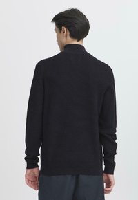 Schwarzer gerippter Pullover mit langen Ärmeln und hohem Kragen, der ein strukturiertes Design und einen geraden Saum an der Taille hat.