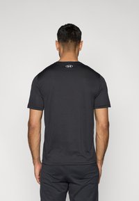 Μαύρο αθλητικό κοντομάνικο μπλουζάκι με στρογγυλή λαιμόκοψη και αντίθετο λογότυπο στο πίσω μέρος· λεία υφή με ύφασμα που απομακρύνει την υγρασία.