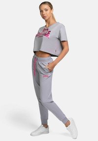 Grå kortärmad tröja med rosa logotyp, kombinerad med grå sweatpants med rosa detaljer och sidofickor, kompletterad med vita sneakers.