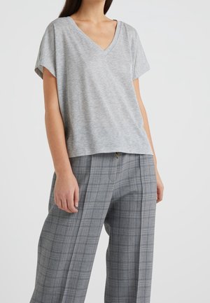 Kobieta ubrana w jasnoszary krótki top z dekoltem w serek, zestawiony z szarymi szerokimi spodniami w kratę na jednolitym tle.