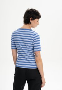 Blue and white striped short-sleeve shirt with a ribbed texture, featuring a round neckline and a fitted shape. Worn with black pants.