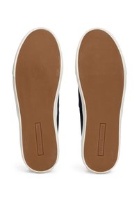 Semelles de baskets avec une surface en caoutchouc texturée couleur tan et des bords blancs. Logo "TOMMY HILFIGER" embossé sur la partie marron.