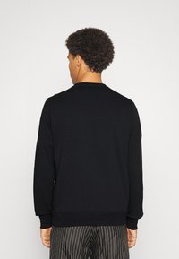 Felpa nera con maniche lunghe, polsini e scollo a coste, mostrata sul retro. Presenta un tessuto liscio e strutturato.