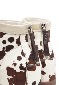 Enkellaarzen van koeienhuid met een wit-bruine print, lederen accenten en zichtbare ritsen met decoratieve trekker.