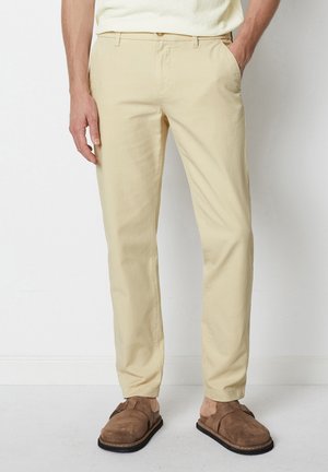 Beige cotton chinos with a slim fit, featuring side pockets and belt loops, paired with brown suede clogs.