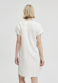 Weißes Leinenkleid mit kurzen Ärmeln, lockerer Passform und abgerundetem Saum. Verfügt über ein Joch-Detail am Rücken für zusätzlichen Blickfang.