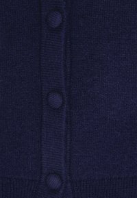 Nærbillede af et mørkeblåt strikket stof med tre beklædte knapper arrangeret lodret langs en ribbet kant.