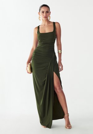 Oliwkowa, długa do podłogi sukienka z dopasowanym gorsetem, kwadratowym dekoltem, marszczeniami po bokach i wysokim rozcięciem. Dopasowana do złotych dodatków.