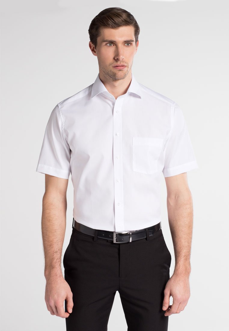Hvid kortærmet skjorte med knaplukning og brystlomme, lavet af glatstof, kombineret med sorte bukser og et tyndt sort bælte.