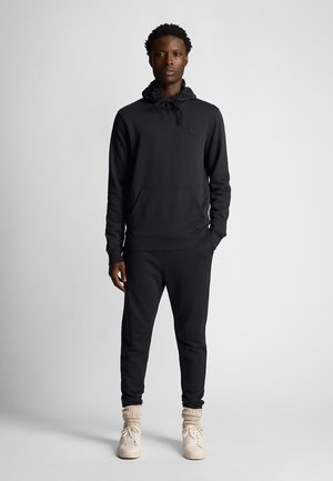 Sweat à capuche noir et joggeurs assortis en tissu doux. Le sweat à capuche est doté d'une poche kangourou et d'un cordon de serrage. Des baskets viennent parfaire le look.