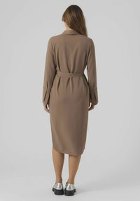 Brun långärmad klänning med bälte i midjan, som har rak skärning och knäppning vid ärmsluten. Bärs med silvriga platåskor.
