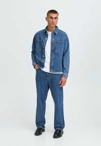 Denim jakna i hlače srednje plave boje s dva prednja džepa. Nosivo s bijelom majicom i crnim cipelama. Glatka tekstura, ležeran kroj.