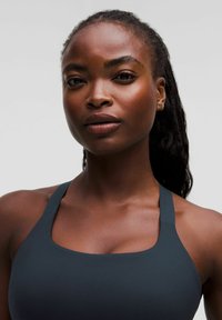 Mörkgrå sportbehå med en jämn textur, breda axelband och en rundad halsringning. Enkel, funktionell estetik utan ytterligare mönster.